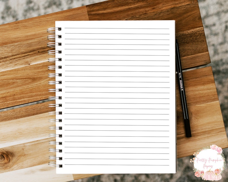 Pode incluir: Um caderno branco de espiral com p&aacute;ginas pautadas e uma caneta preta sobre uma superf&iacute;cie de madeira.