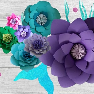 May include: A collection of paper flowers in various colors, including purple, teal, green, and pink. The flowers are arranged on a white wooden background with a teal and silver mermaid tail.