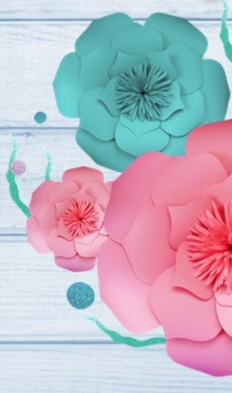 May include: Three large paper flowers, one teal blue and two pink, with a wood background. The flowers are layered and have a ruffled appearance.