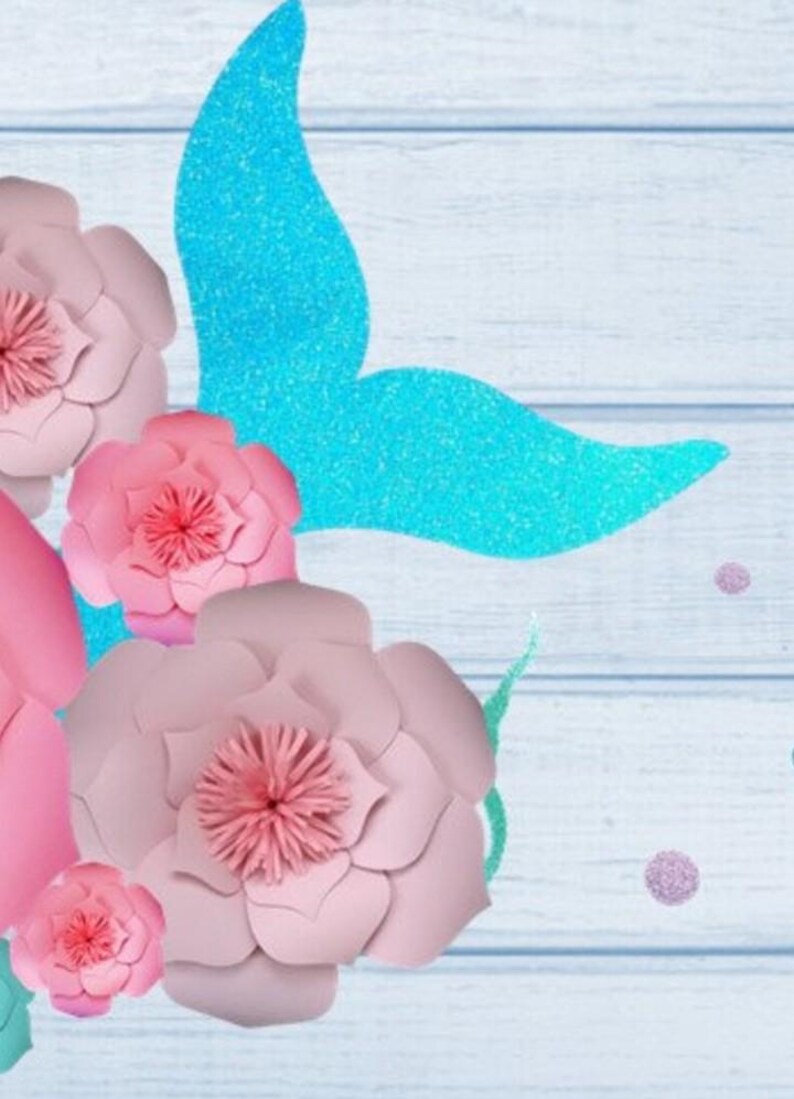 May include: Pink paper flowers with a blue glitter mermaid tail on a light blue wooden background.