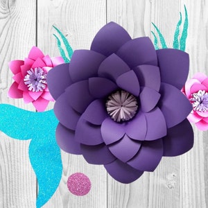 May include: Purple, pink, and blue paper flowers with glitter accents on a white wood background.