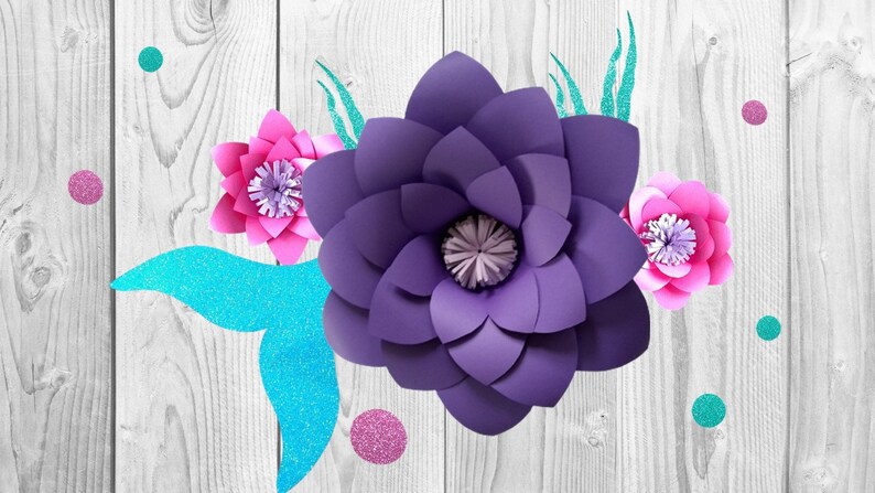 May include: Purple, pink, and blue paper flowers with glitter accents on a white wood background.
