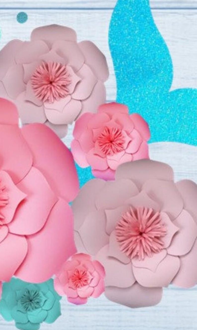 May include: A set of pink and teal paper flowers. The flowers are layered and have a ruffled texture. The flowers are arranged on a blue and white background.