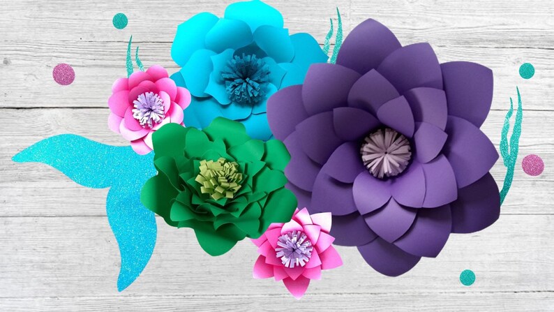 May include: A set of five paper flowers in various colors, including teal, purple, pink, and green. The flowers are arranged on a white wooden background.