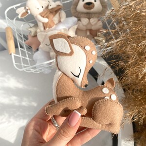 May include: A brown felt deer with white spots and closed eyes. The deer is lying down with its head turned to the side. The deer is a handmade toy.