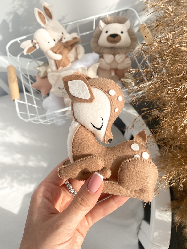 May include: A brown felt deer with white spots and closed eyes. The deer is lying down with its head turned to the side. The deer is a handmade toy.