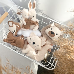 May include: A white wire basket filled with plush animal toys. The toys include a brown deer, a white cat, a brown rabbit, a white rabbit, and a brown and white lion. The toys are all lying down and have embroidered eyes and noses.