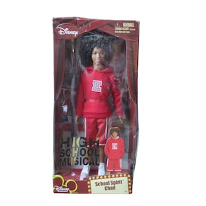 May include: A Disney "High School Musical" doll of the character Chad, in a red sweatsuit with the letter "E". The doll is in a clear plastic package with the movie title and character name printed on the front.