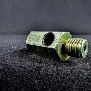 May include: A metal T-shaped fitting with a threaded end and a hole in the center. The fitting is a light green color and has a rough texture.