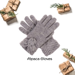 Op de afbeelding: Een paar grijze alpaca handschoenen met een bloemdetail op de manchet. De handschoenen zijn dubbelgevouwen en de tekst "Alpaca Gloves" staat eronder.