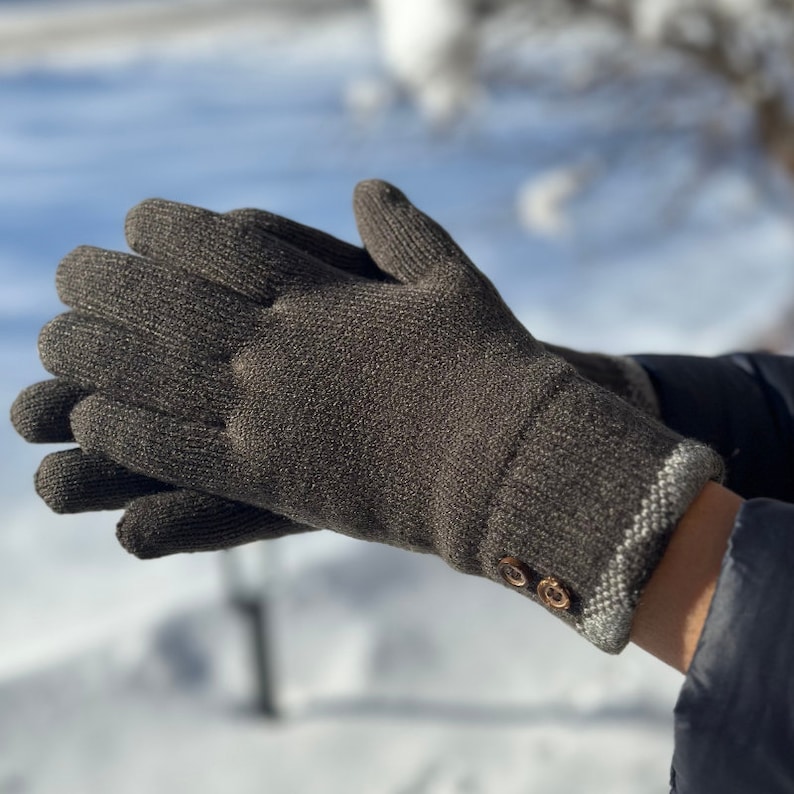 May include: A pair of brown knit gloves with a white trim and two brown buttons on the cuff.