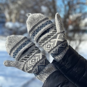 May include: A pair of grey and blue patterned mittens with a fold-over cuff. The mittens are made of a soft, knitted fabric and have a geometric design.