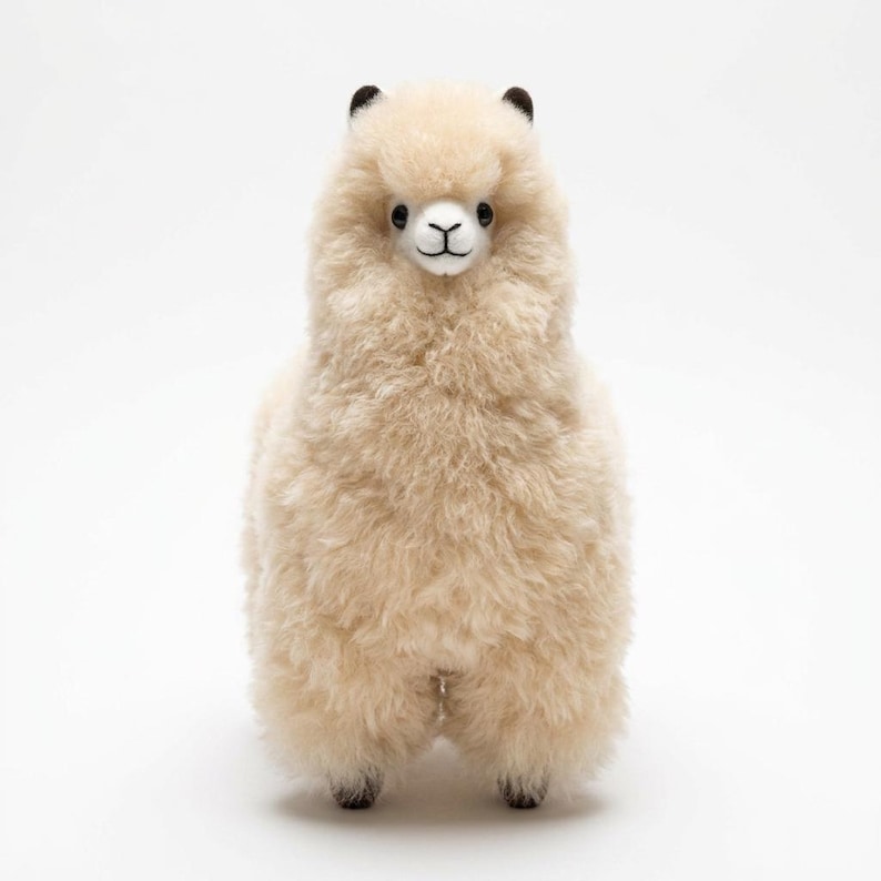 Op de afbeelding: Een staand alpaca-knuffel met een cr&egrave;mekleurig, pluizig lichaam. De alpaca heeft zwarte ogen, een wit gezicht en kleine zwarte oren. Het speelgoed is ontworpen om op een echte alpaca te lijken.