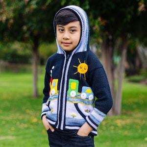 May include: A blue knitted hoodie with a zipper closure, featuring a colorful train design and a smiling sun applique. The hoodie has a white and blue striped trim.