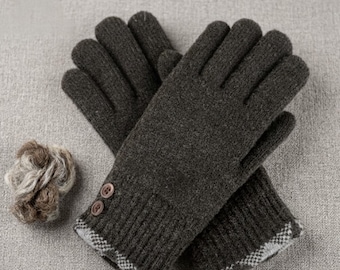May include: A pair of dark brown knit gloves featuring a ribbed cuff, two small brown buttons on the side of the wrist, and a grey and white checkered pattern along the bottom edge. A small, textured ball of matching brown yarn sits nearby.