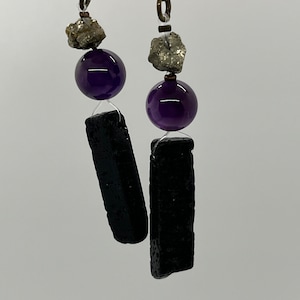 Puede incluir: Un par de pendientes colgantes con roca de lava negra, cuentas de amatista y detalles de pirita.