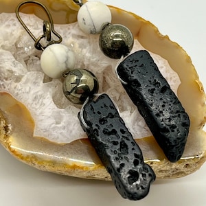 Puede incluir: Un par de pendientes con roca de lava negra, cuentas de mármol blanco y negro y cuentas de pirita dorada.