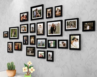 May include: A gallery wall with 20 black picture frames of various sizes, each containing a photograph of a couple. The frames are arranged in a staggered pattern on a white wall. A small potted plant sits on a shelf below the frames.