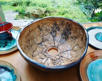 May include: A ceramic sink with a unique design featuring a tree branch pattern in black and brown on a beige background. The sink has a round shape and a hole in the center.