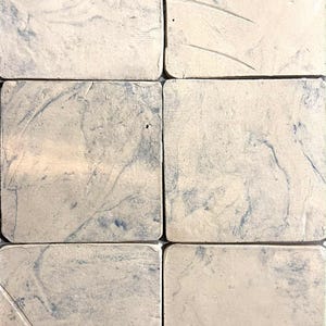 Może przedstawiać: Sześć kwadratowych ceramicznych podkładek z marmurkowym wzorem. Podkładki mają kremową podstawę z niebieskimi żyłkami, tworząc wygląd naturalnego kamienia. Podkładki są ułożone w siatkę, prezentując swoje indywidualne wzory.