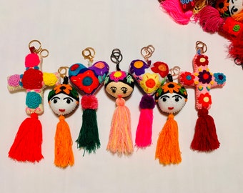 May include: A collection of colorful handmade keychains featuring felt designs. The keychains include cross and heart shapes, and Frida Kahlo-inspired faces. Each keychain has a tassel and gold-colored metal ring.