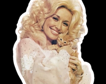 May include: A sticker featuring a smiling woman with voluminous blonde hair, holding a small orange tabby cat. She wears a light pink dress with white lace and sparkling embellishments, set against a black background.