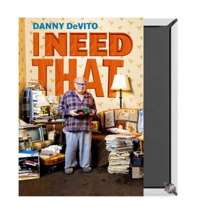 May include: A book cover featuring Danny DeVito with the title "I NEED THAT" in large orange letters. The background is a cluttered room with a lamp, furniture, and stacks of books and magazines.