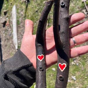May include: Two dark brown wooden handles, possibly for a drawer or cabinet, each with a red heart painted on them. The handles are attached with screws.