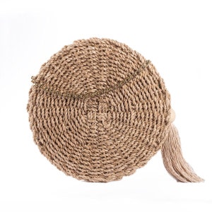 May include: A round, woven handbag in natural beige tones. The bag features a spiral design, a decorative chain, and a tassel. The bag is made of a natural fiber material, and is suitable for carrying essentials.