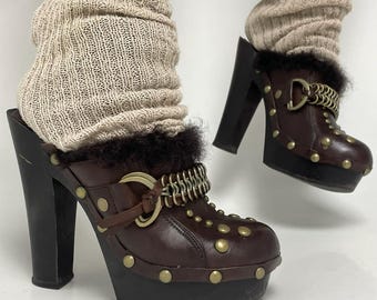 May include: Brown leather platform clogs with a black sole and heel. The clogs feature gold-colored studs, a chain detail, and a fur trim. The heels are approximately 4 inches high.