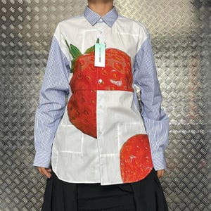 Peut inclure: Chemise blanche à manches rayées bleues et col, ornée d'une grande fraise rouge imprimée sur le devant. La chemise est de style boutonné et porte une étiquette.