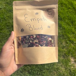 Puede incluir: Una bolsa de papel marrón con una etiqueta escrita a mano que dice "Empath Blend". La bolsa contiene hierbas y flores secas. Una pegatina en la bolsa dice "¡Gracias! -Simon".