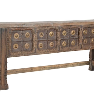 May include: A long, rectangular wooden console table featuring a weathered brown finish. The front panel is decorated with sixteen square sections, each centered with a circular brass-toned metal accent. The table stands on four carved legs.