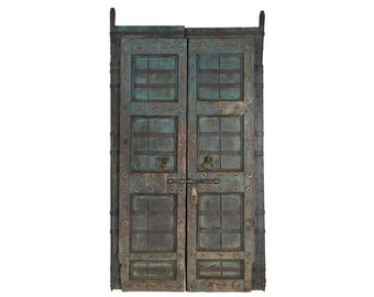 Könnte beinhalten: Ein Paar verwitterte, blaugrüne Holztüren mit Paneeldesign, dunklen horizontalen Metallverstrebungen und runden Metallnieten. Die Türen sind mit messingfarbenen Ringgriffen und einem zentralen horizontalen Schieberiegel-Verschlussmechanismus ausgestattet.
