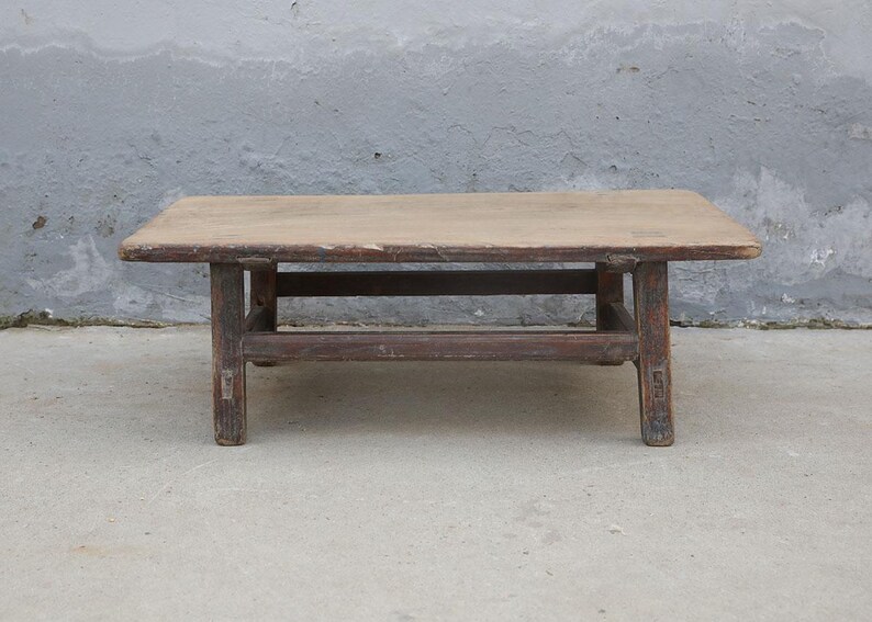 May include: A low rectangular wooden coffee table with a weathered brown finish. The table features a flat, smooth top surface supported by four sturdy legs connected by horizontal wooden stretchers, showing visible signs of age and wear.