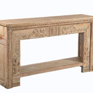 May include: A rectangular wooden console table featuring intricate hand-carved floral and geometric patterns along the front frame and side panels. The piece has a flat top surface, a single open lower shelf, and a natural light brown wood finish.