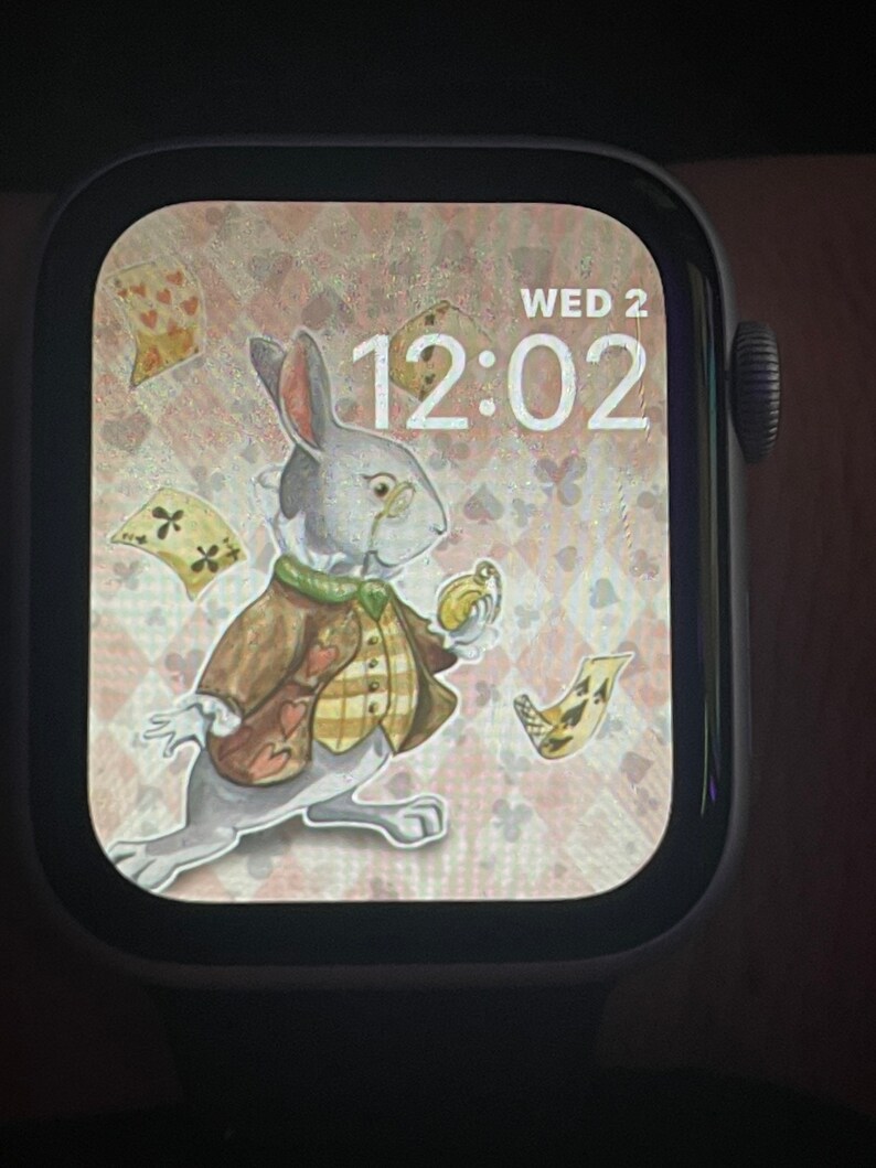 Puede incluir: Un conejo blanco con chaleco y sosteniendo un reloj de bolsillo, con un fondo rosa y blanco con cartas de juego. La hora en la esfera del reloj es 12:02 y el d&iacute;a es Mi&eacute; 2.