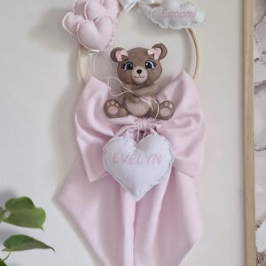 Può includere: Decorazione per la cameretta fatta a mano con un orsetto marrone, fiocchi rosa e un cartello a forma di cuore con "EVELYN". Include anche palloncini rosa a forma di cuore e una nuvola con il nome "Eccomi".