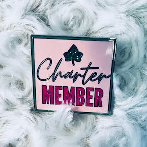 May include: A pink and green enamel pin with a green leaf and the text "Charter Member" in black and pink lettering.