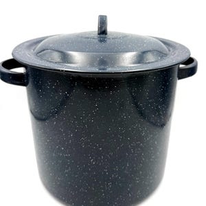 Op de afbeelding: Een diepe, cilindrische soeppan met bijpassend deksel, afgewerkt in donkerblauw emaille met een wit gespikkeld patroon. De pan is voorzien van twee zijhandgrepen en een centrale knop op het deksel, wat zorgt voor een functioneel ontwerp.