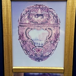 May include: A framed print of an ornate, egg-shaped object featuring intricate scrollwork, embedded jewels, and the year 1903. The central panel displays a landscape scene, while the text "1903" and Cyrillic lettering are visible on the surface.