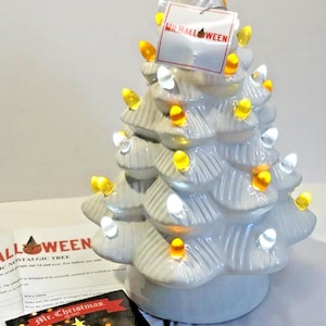 Può includere: Un albero di Halloween in ceramica con una copertura di caramelle di mais e luci colorate. L'albero ha un'etichetta con la scritta "Mr. Halloween". Una carta con un disegno di albero di Natale è di fronte all'albero.