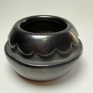 Puede incluir: Un cuenco de cerámica negra hecho a mano con un diseño de borde festoneado único. El cuenco tiene una base redondeada y un acabado liso y brillante. Esta pieza decorativa es ideal para la decoración del hogar o como objeto funcional.