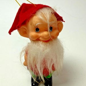 Pode incluir: Enfeite de Natal vintage em forma de gnomo. O gnomo tem um chapéu vermelho, barba branca e sapatos pretos. O enfeite tem um fio dourado para pendurar e é feito de plástico.