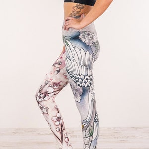 May include: White yoga leggings with a floral and bird print. The leggings have a high waist and a fitted silhouette.