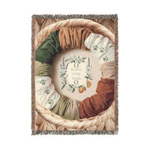 Peut inclure: Plaid tissé avec un motif circulaire bordé d'un panier tressé. Le centre affiche le texte "Bless This Nest" entouré d'illustrations florales et fruitières. Le motif incorpore des couleurs vertes, marron et crème.