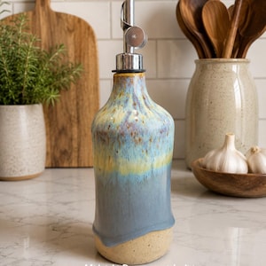Puede incluir: Un dispensador de aceite de cer&aacute;mica con esmalte reactivo en tonos azules, amarillos y marrones. La botella tiene un cuello c&oacute;nico, un vertedor de metal plateado y una base beige moteada. El texto "Midnight Run - special edition" es visible.
