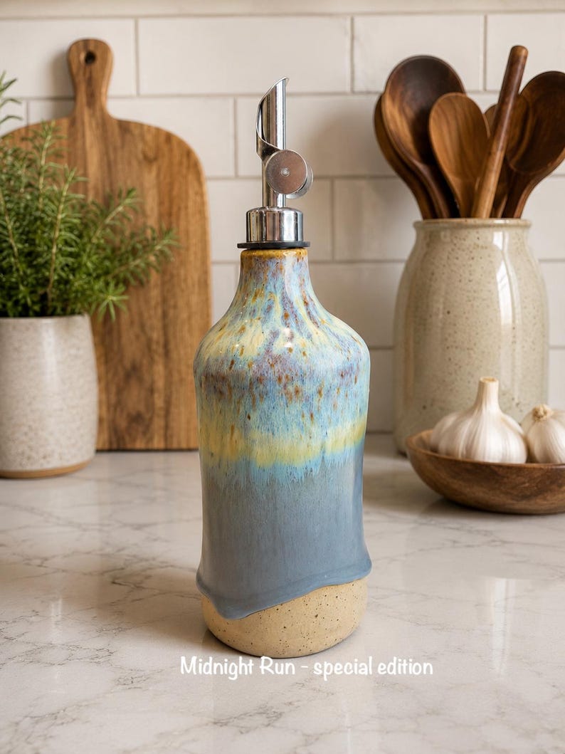 Puede incluir: Un dispensador de aceite de cer&aacute;mica con esmalte reactivo en tonos azules, amarillos y marrones. La botella tiene un cuello c&oacute;nico, un vertedor de metal plateado y una base beige moteada. El texto "Midnight Run - special edition" es visible.