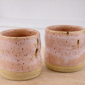 May include: A set of three ceramic mugs with a speckled, cream-colored glaze. Each mug features a different hand-painted floral design in shades of blue, green, and yellow. The mugs have a simple, modern shape.