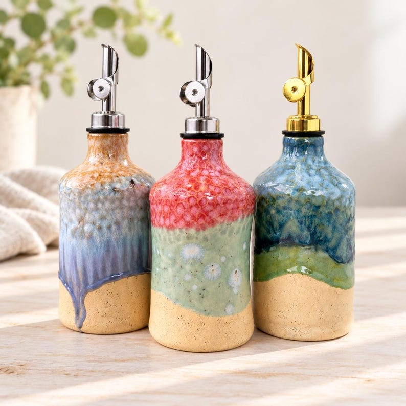 Puede incluir: Tres dispensadores de aceite de cer&aacute;mica con acabados de esmalte texturizado multicolor. Cada botella cuenta con un vertedor met&aacute;lico, dos plateados y uno dorado, sobre una base cil&iacute;ndrica con una parte inferior beige moteada.